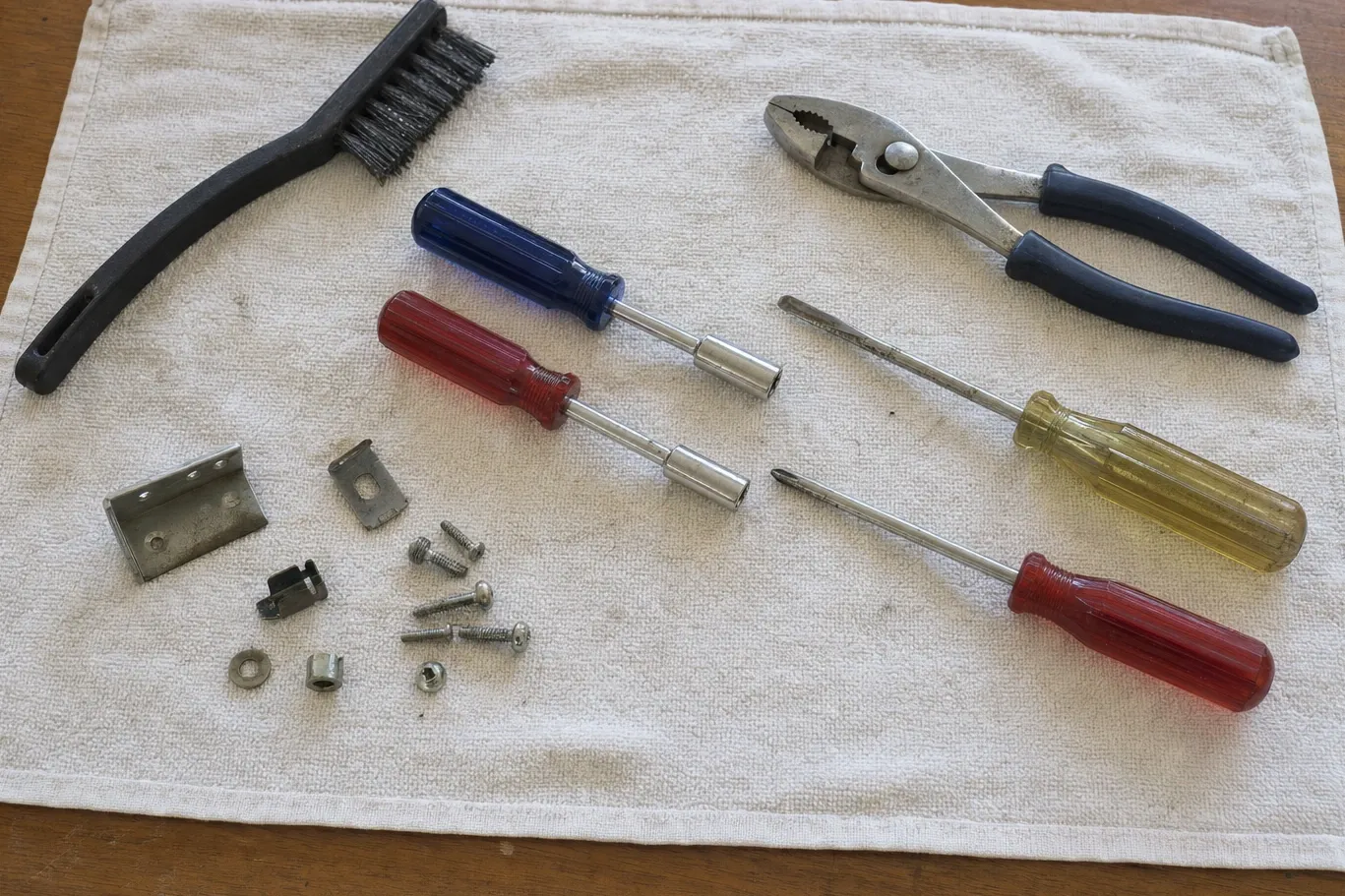 Hex nut drivers, slip-joint pliers, screwdrivers, a bracket and loose fixings laid out on a folded towel